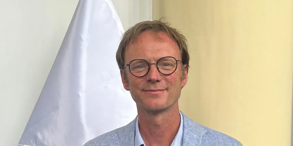 Portrait photo of Dr Chris Butler facing camera with flag behind